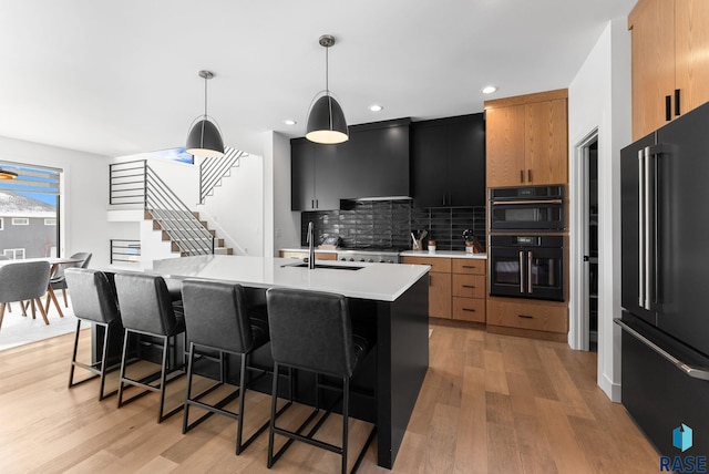 kitchen with hanging light fixtures, an island with sink, black appliances, tasteful backsplash, and sink