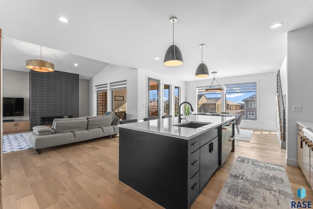 kitchen featuring dishwasher, pendant lighting, a tile fireplace, an island with sink, and sink