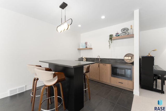 kitchen featuring a breakfast bar area, built in microwave, pendant lighting, light brown cabinetry, and sink