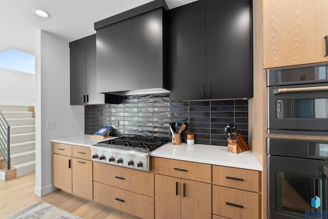 kitchen featuring light wood-type flooring, double oven, stainless steel gas stovetop, wall chimney range hood, and backsplash