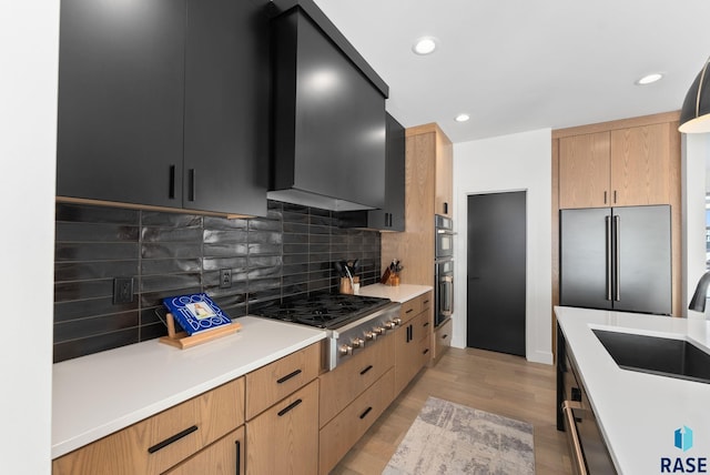 kitchen with wall chimney exhaust hood, stainless steel appliances, light hardwood / wood-style floors, decorative backsplash, and sink