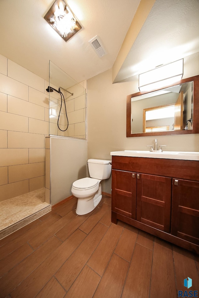 bathroom featuring toilet, a tile shower, wood-type flooring, and vanity