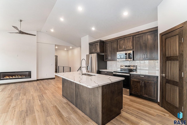 kitchen with stainless steel appliances, a center island with sink, decorative backsplash, lofted ceiling, and light wood-type flooring