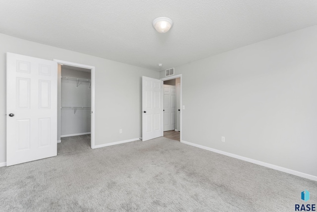 unfurnished bedroom with a textured ceiling, light colored carpet, a closet, and a walk in closet