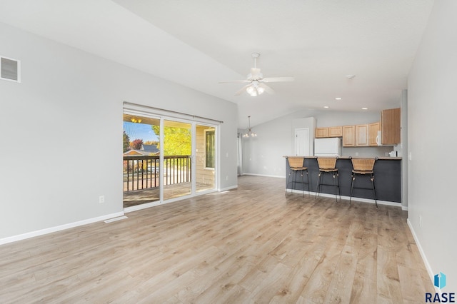 unfurnished living room with ceiling fan with notable chandelier, light wood-type flooring, and vaulted ceiling