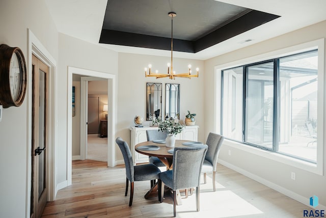 dining room with an inviting chandelier, light wood-type flooring, and a tray ceiling