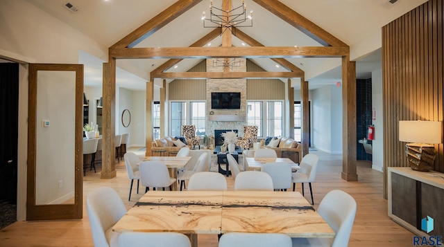 dining space featuring a notable chandelier, light hardwood / wood-style floors, high vaulted ceiling, beamed ceiling, and a stone fireplace