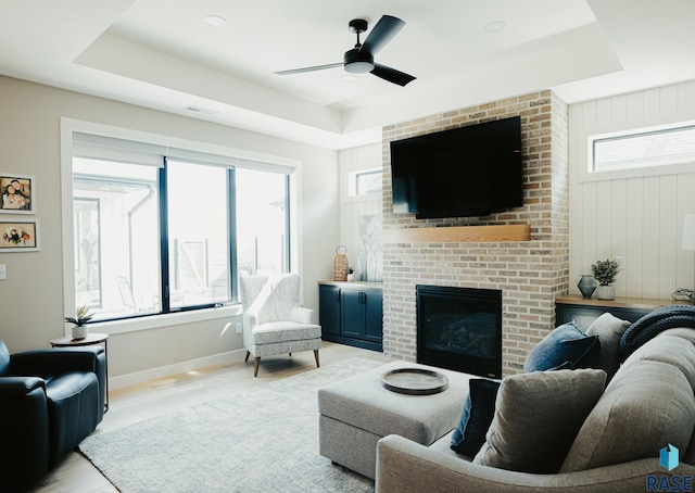 living room with ceiling fan, a tray ceiling, and light hardwood / wood-style floors