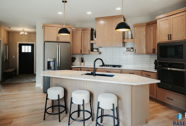 kitchen with black appliances, pendant lighting, an island with sink, and light stone counters