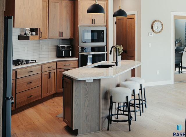 kitchen with light wood-type flooring, black appliances, decorative backsplash, hanging light fixtures, and a kitchen island with sink