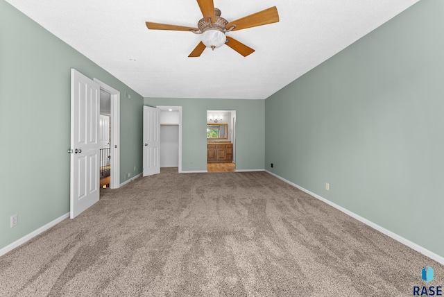 unfurnished bedroom with a walk in closet, carpet, connected bathroom, and ceiling fan