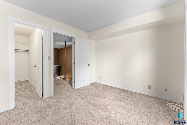 unfurnished bedroom featuring a walk in closet, a closet, and light colored carpet