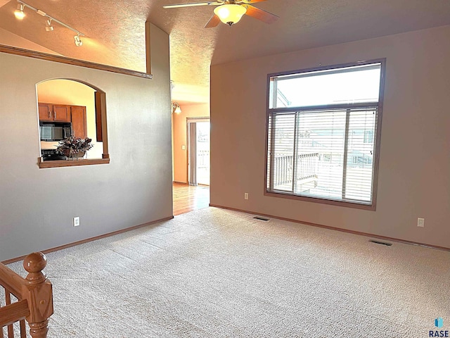 carpeted spare room featuring ceiling fan, vaulted ceiling, a textured ceiling, and rail lighting