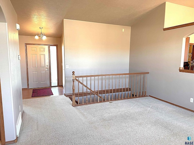 entrance foyer with an inviting chandelier, carpet floors, vaulted ceiling, and a textured ceiling