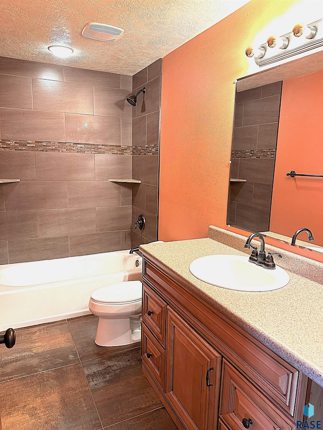 full bathroom featuring a textured ceiling, tiled shower / bath combo, vanity, and toilet