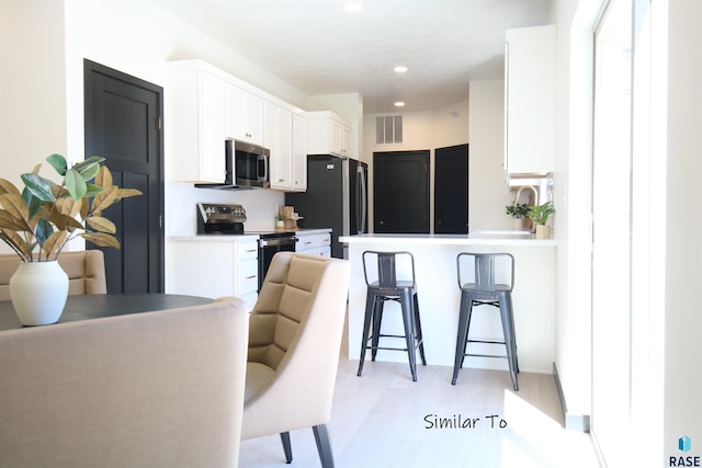 kitchen featuring stainless steel appliances, white cabinets, a breakfast bar, and light hardwood / wood-style flooring