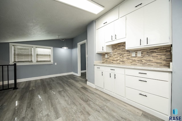 kitchen with wood-type flooring, a textured ceiling, white cabinetry, lofted ceiling, and tasteful backsplash