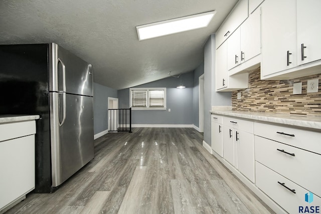 kitchen featuring white cabinets, a textured ceiling, lofted ceiling, decorative backsplash, and stainless steel fridge