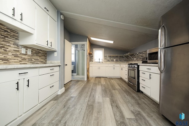 kitchen featuring lofted ceiling, white cabinets, backsplash, and appliances with stainless steel finishes