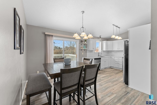 dining area with sink, a textured ceiling, vaulted ceiling, light wood-type flooring, and a notable chandelier