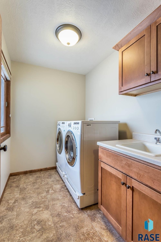 clothes washing area with sink, washing machine and dryer, a textured ceiling, and cabinets