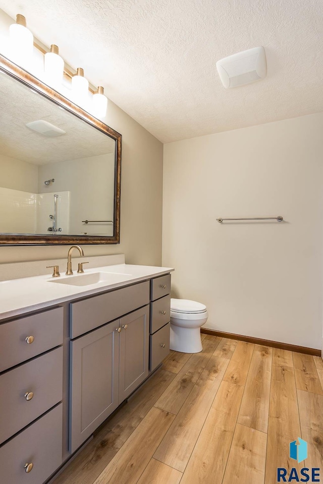 bathroom featuring a textured ceiling, hardwood / wood-style floors, toilet, walk in shower, and vanity