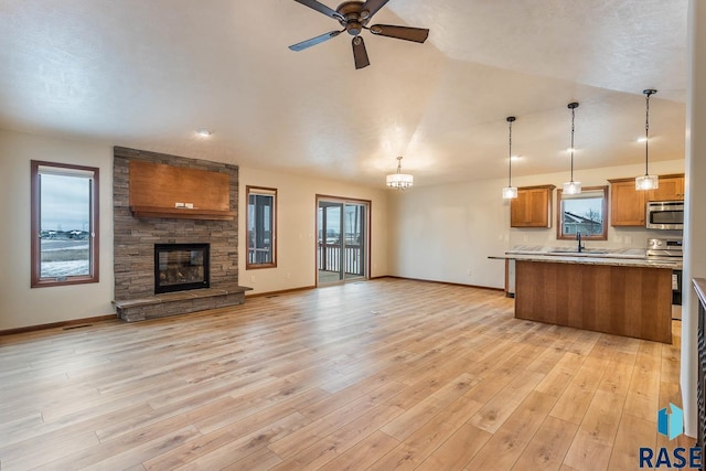 kitchen with a stone fireplace, appliances with stainless steel finishes, light wood-type flooring, ceiling fan, and decorative light fixtures