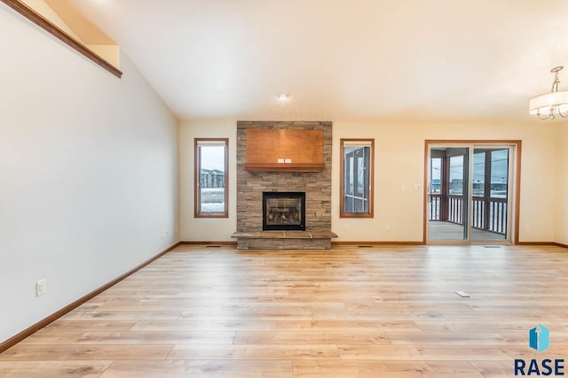 unfurnished living room featuring lofted ceiling, a fireplace, a notable chandelier, and light hardwood / wood-style flooring