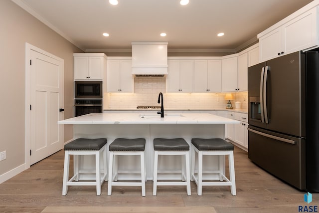 kitchen with black appliances, custom exhaust hood, an island with sink, and white cabinets