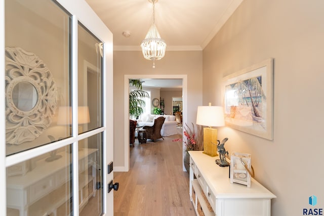 hallway with ornamental molding, light wood-type flooring, and a chandelier