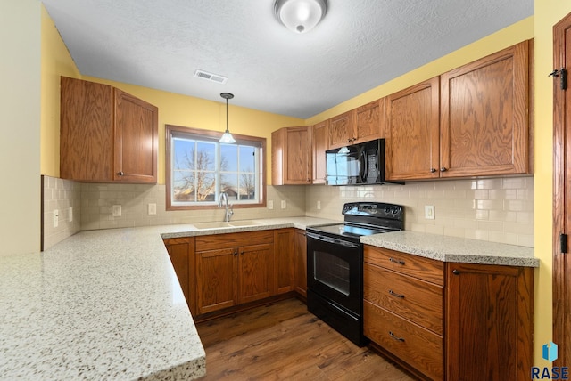 kitchen with black appliances, decorative backsplash, sink, hanging light fixtures, and light stone counters