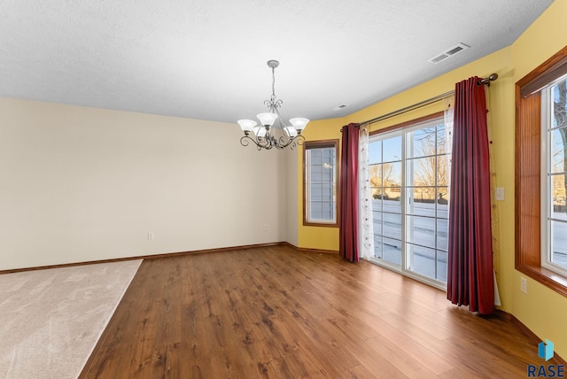 unfurnished dining area with hardwood / wood-style floors, a textured ceiling, and an inviting chandelier