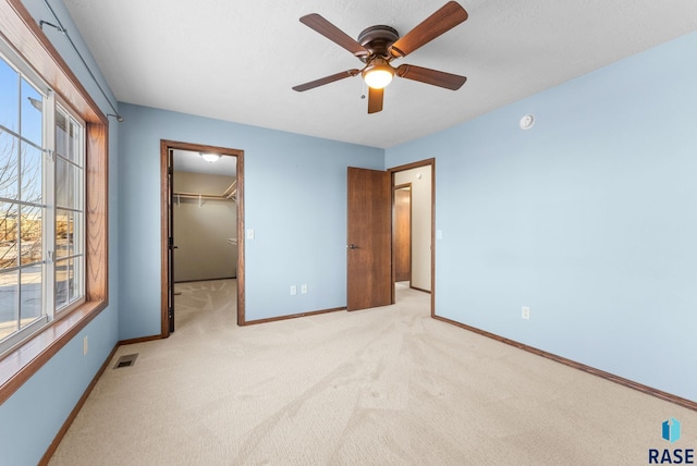 unfurnished bedroom featuring a spacious closet, ceiling fan, a closet, and light carpet