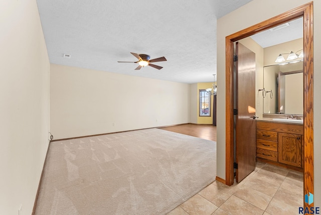 carpeted empty room featuring a textured ceiling, ceiling fan with notable chandelier, and sink