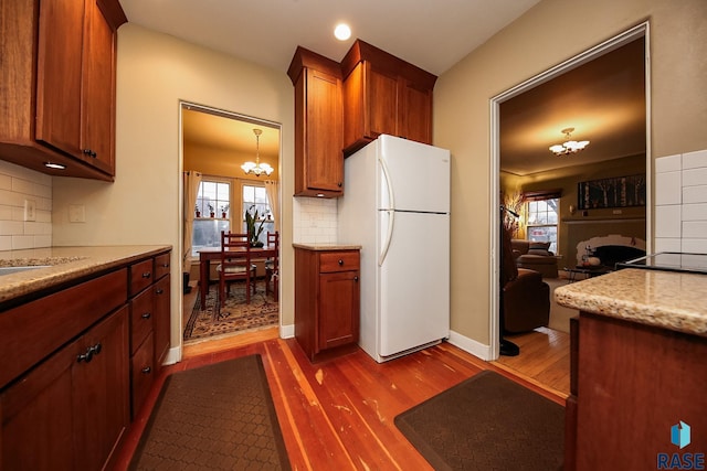 kitchen featuring decorative backsplash, dark wood-type flooring, white refrigerator, and a notable chandelier