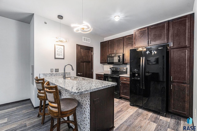 kitchen featuring kitchen peninsula, decorative light fixtures, black appliances, a breakfast bar, and sink