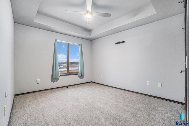 carpeted spare room featuring ceiling fan and a raised ceiling