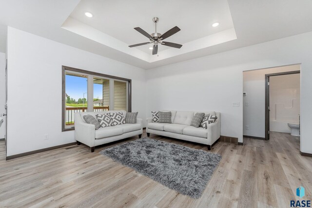 living room with ceiling fan, a tray ceiling, and light hardwood / wood-style flooring