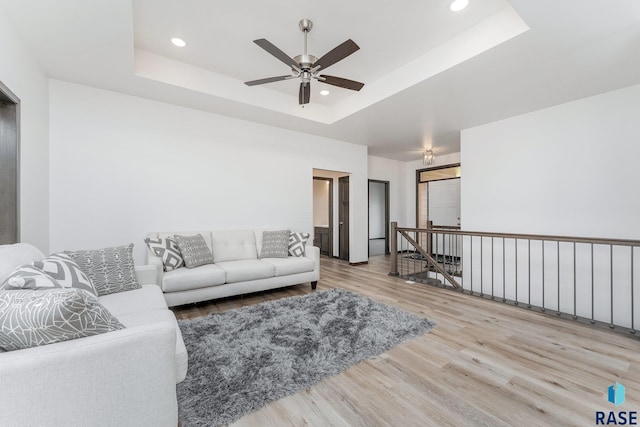 living room featuring hardwood / wood-style flooring, a raised ceiling, and ceiling fan