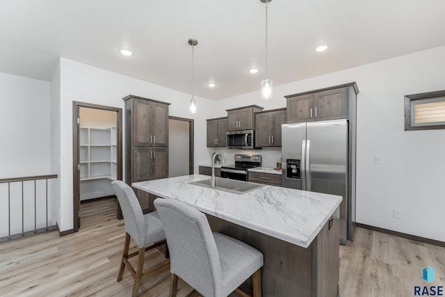 kitchen featuring a center island with sink, appliances with stainless steel finishes, light wood-type flooring, hanging light fixtures, and sink