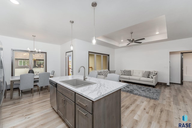 kitchen featuring dishwasher, decorative light fixtures, sink, a tray ceiling, and a center island with sink