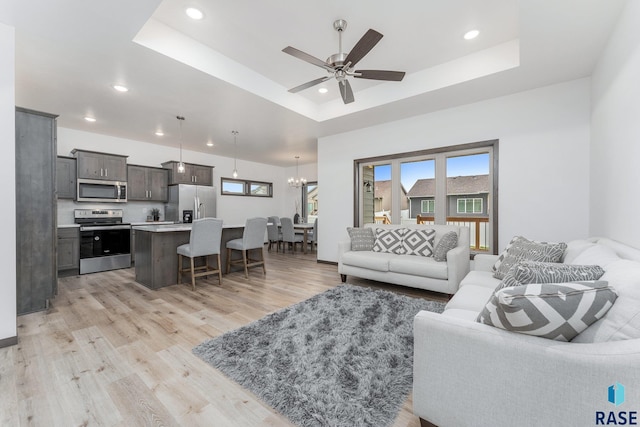 living room with light hardwood / wood-style floors, a raised ceiling, and ceiling fan with notable chandelier