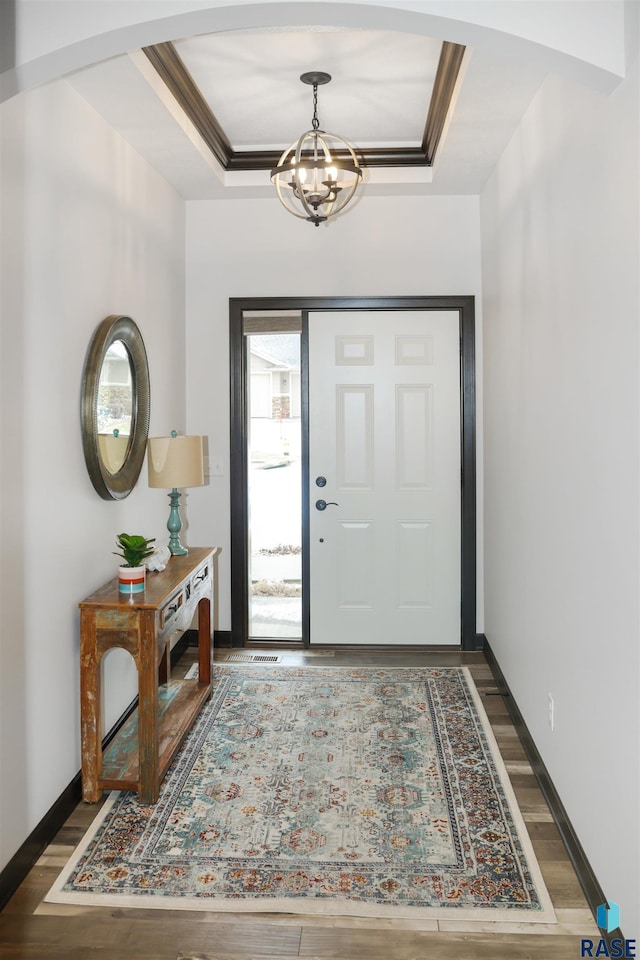 entrance foyer with dark hardwood / wood-style flooring, a tray ceiling, a chandelier, and ornamental molding