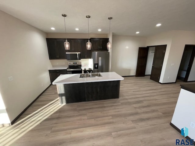 kitchen featuring decorative light fixtures, a center island with sink, sink, light wood-type flooring, and stainless steel appliances