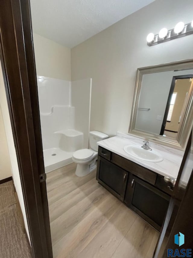 bathroom featuring toilet, vanity, a shower, and hardwood / wood-style floors