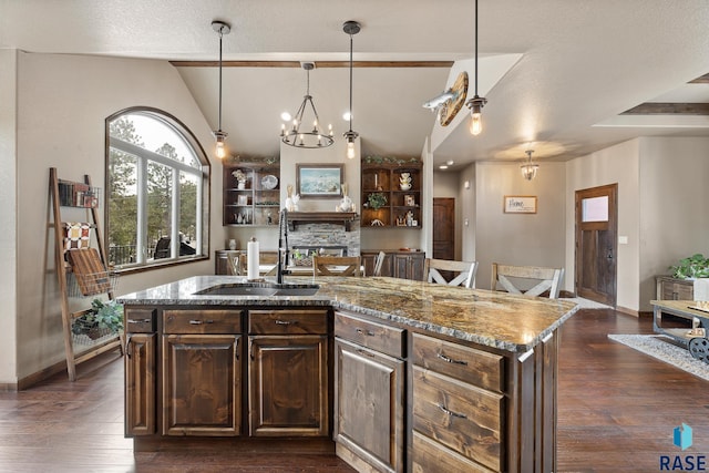 kitchen with sink, vaulted ceiling with beams, an inviting chandelier, light stone countertops, and a kitchen island with sink