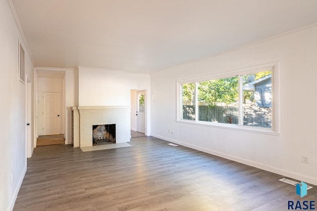 unfurnished living room featuring a brick fireplace, ornamental molding, and hardwood / wood-style floors