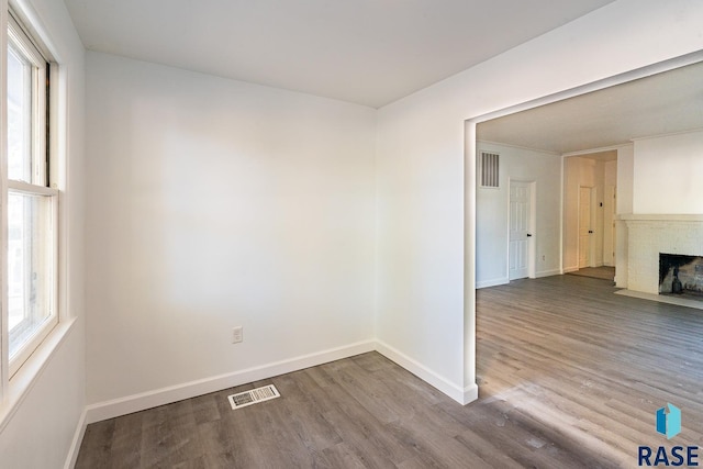 spare room with a brick fireplace, a wealth of natural light, and hardwood / wood-style floors