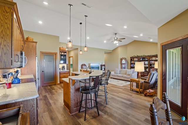 kitchen with an island with sink, ceiling fan, hanging light fixtures, vaulted ceiling, and hardwood / wood-style flooring