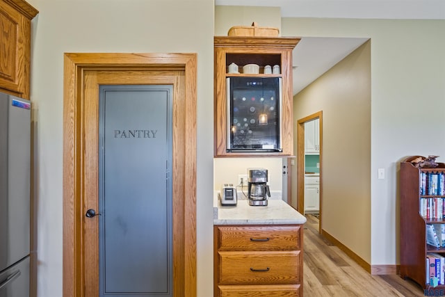 bar featuring light wood-type flooring and stainless steel refrigerator